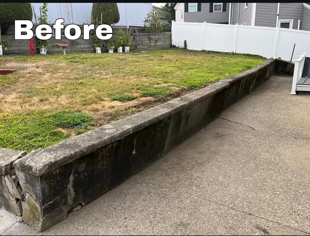 Weathered concrete retaining wall with dark staining separating lawn from patio, before restoration