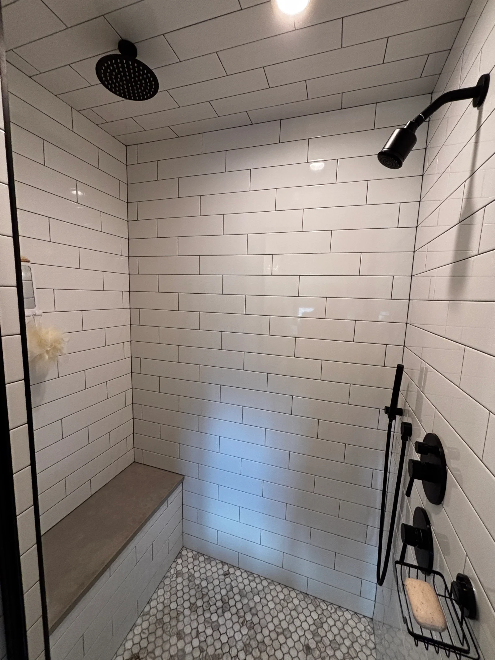 Walk-in shower with white subway tile, dark grout, built-in tile bench, hexagonal mosaic floor, and matte black fixtures