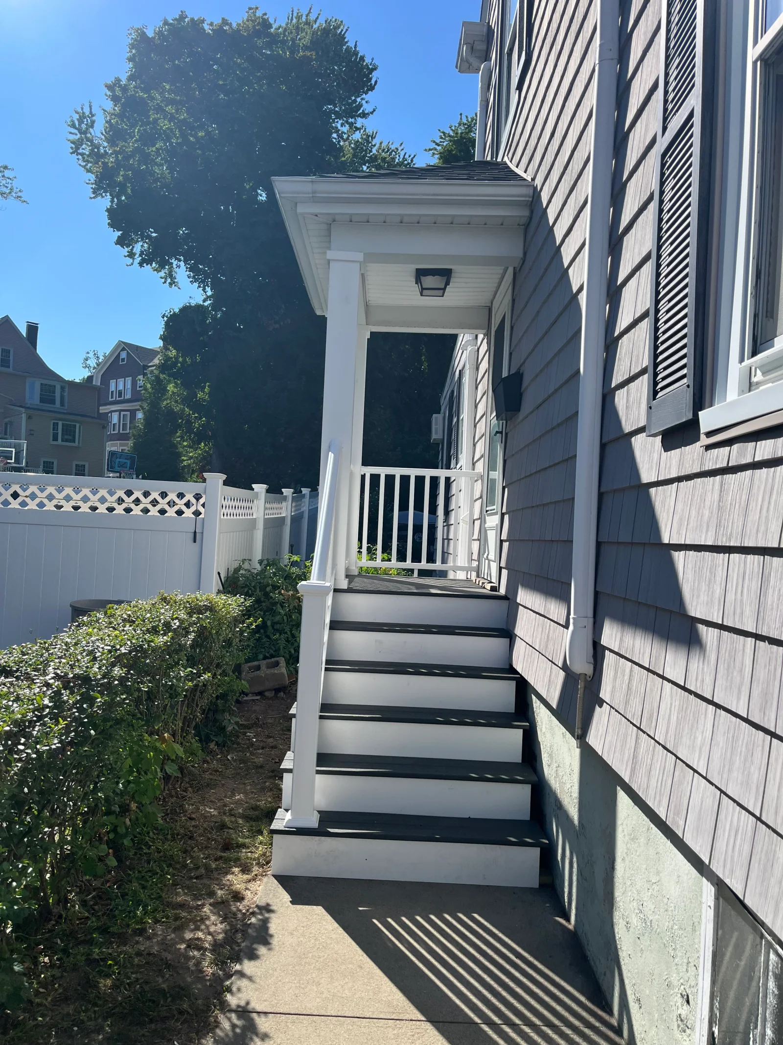 Side entry porch with white risers, dark gray composite treads, white vinyl railing, and covered entry roof