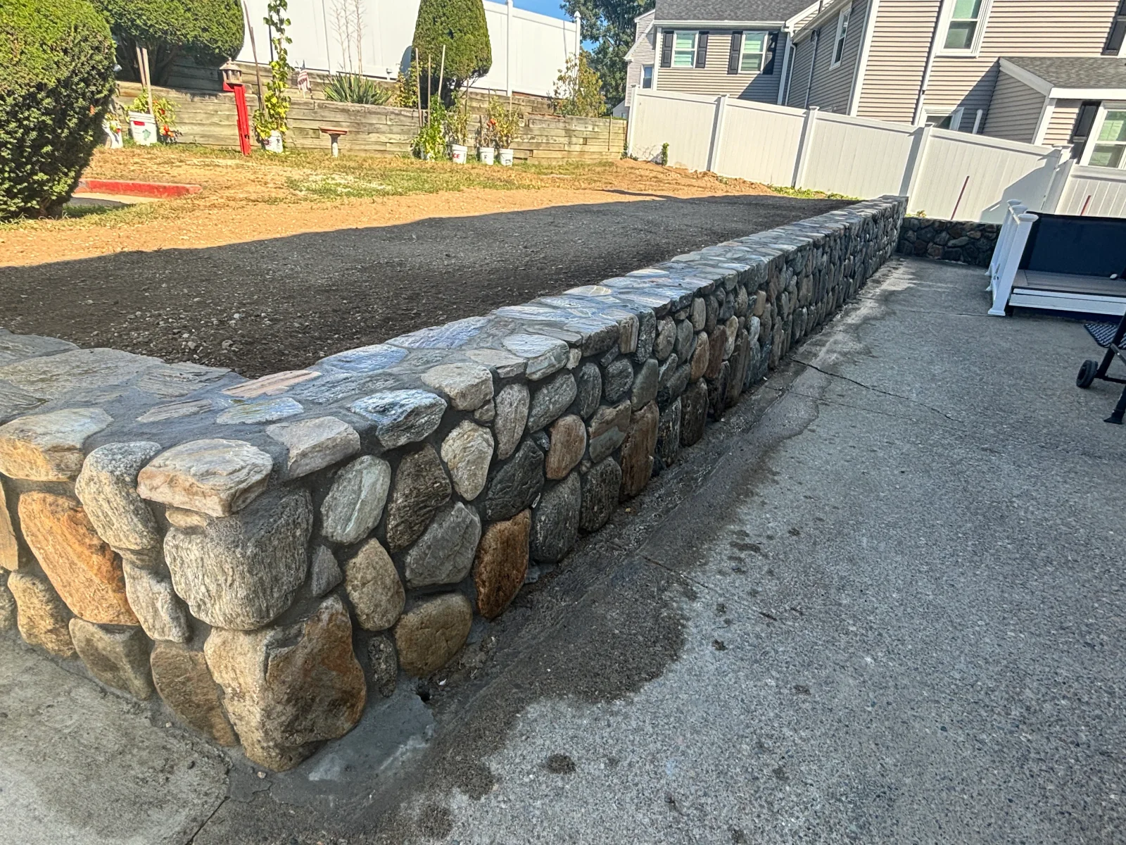 Stacked fieldstone retaining wall with mixed gray and rust-toned boulders and flat cap stones beside a graded yard
