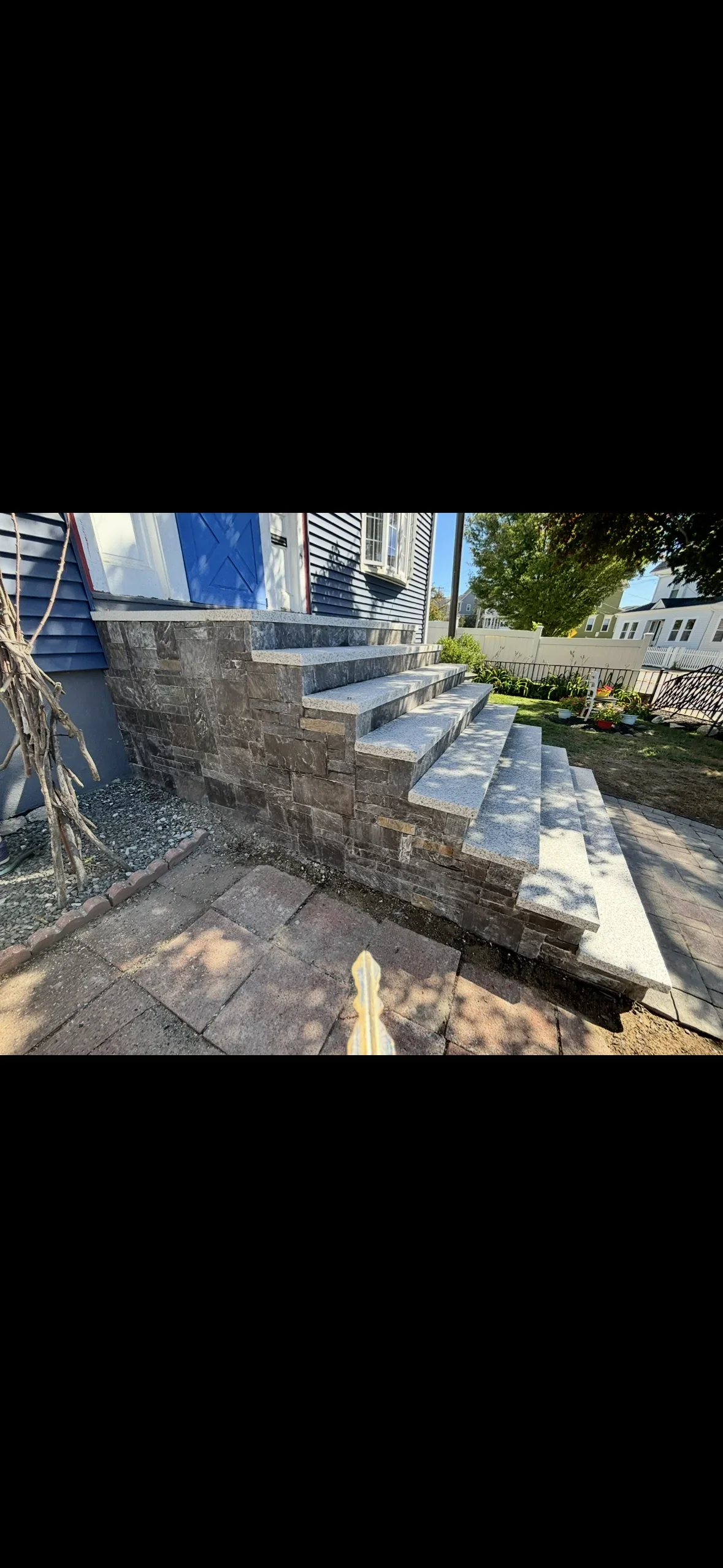 Stone veneer front steps with light gray granite treads and bullnose edges beside a blue house entry