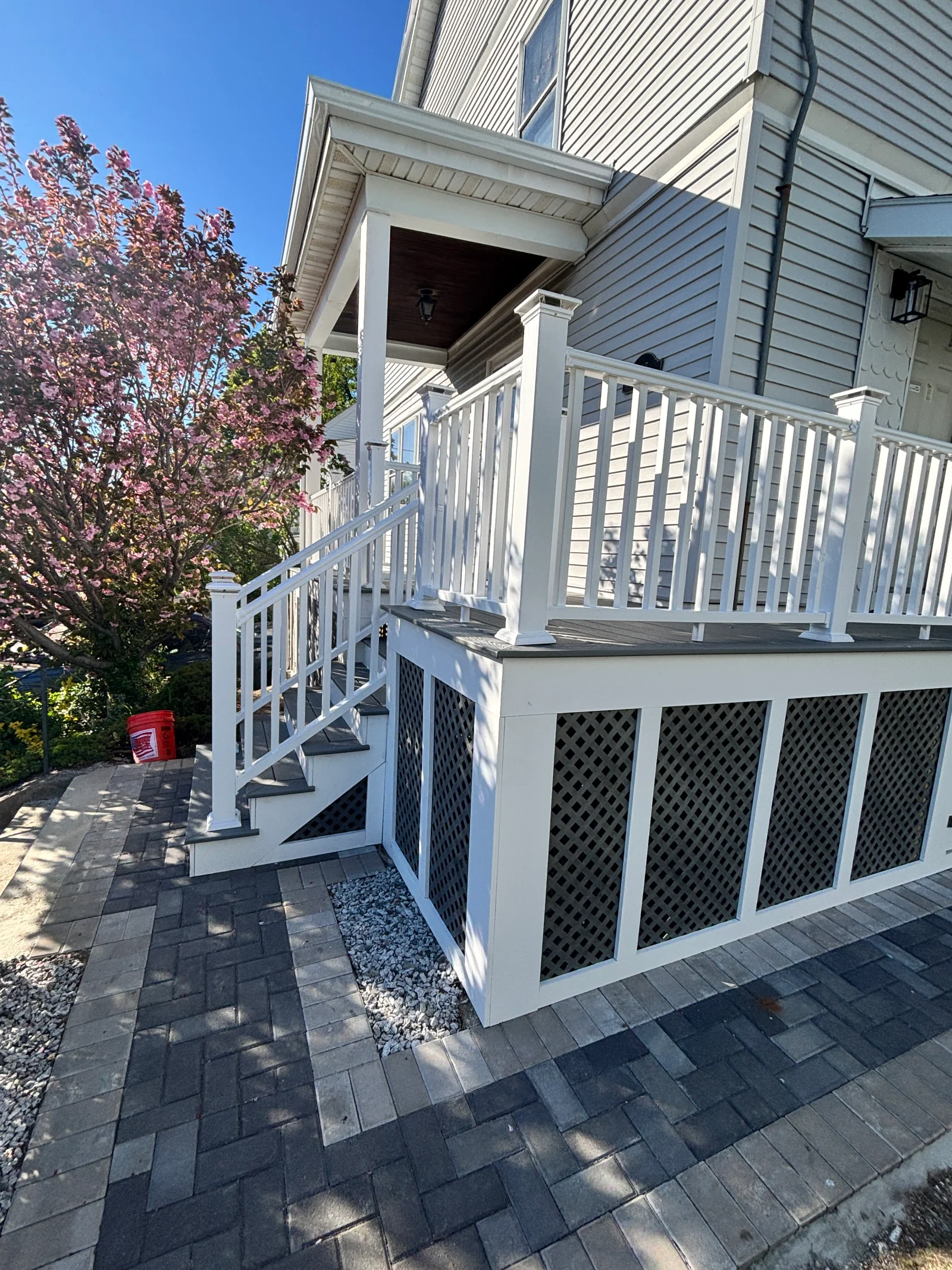 White vinyl railing and gray lattice-skirted porch deck with stairs leading to paver walkway