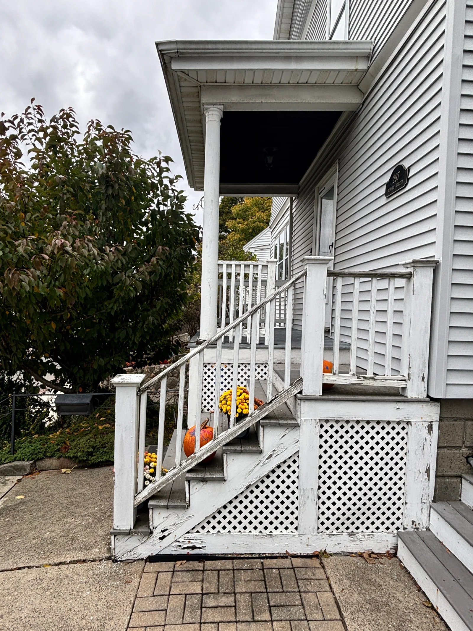 Weathered white wood porch staircase with peeling paint, square newel posts, balusters, and diagonal lattice skirting