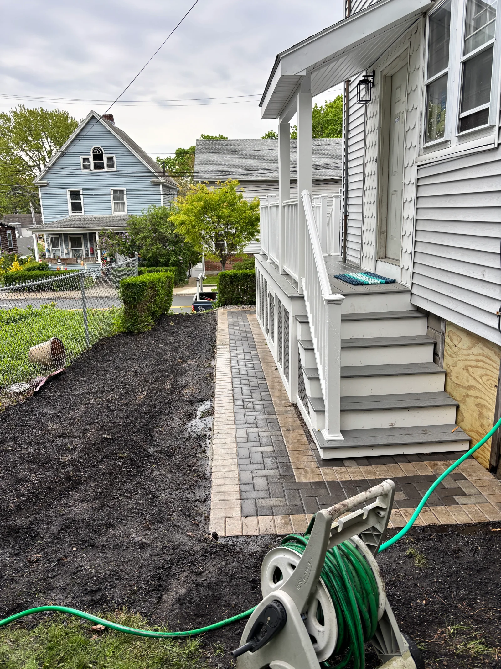 Paver walkway in gray herringbone with tan border beside white porch steps with gray treads and vinyl railing