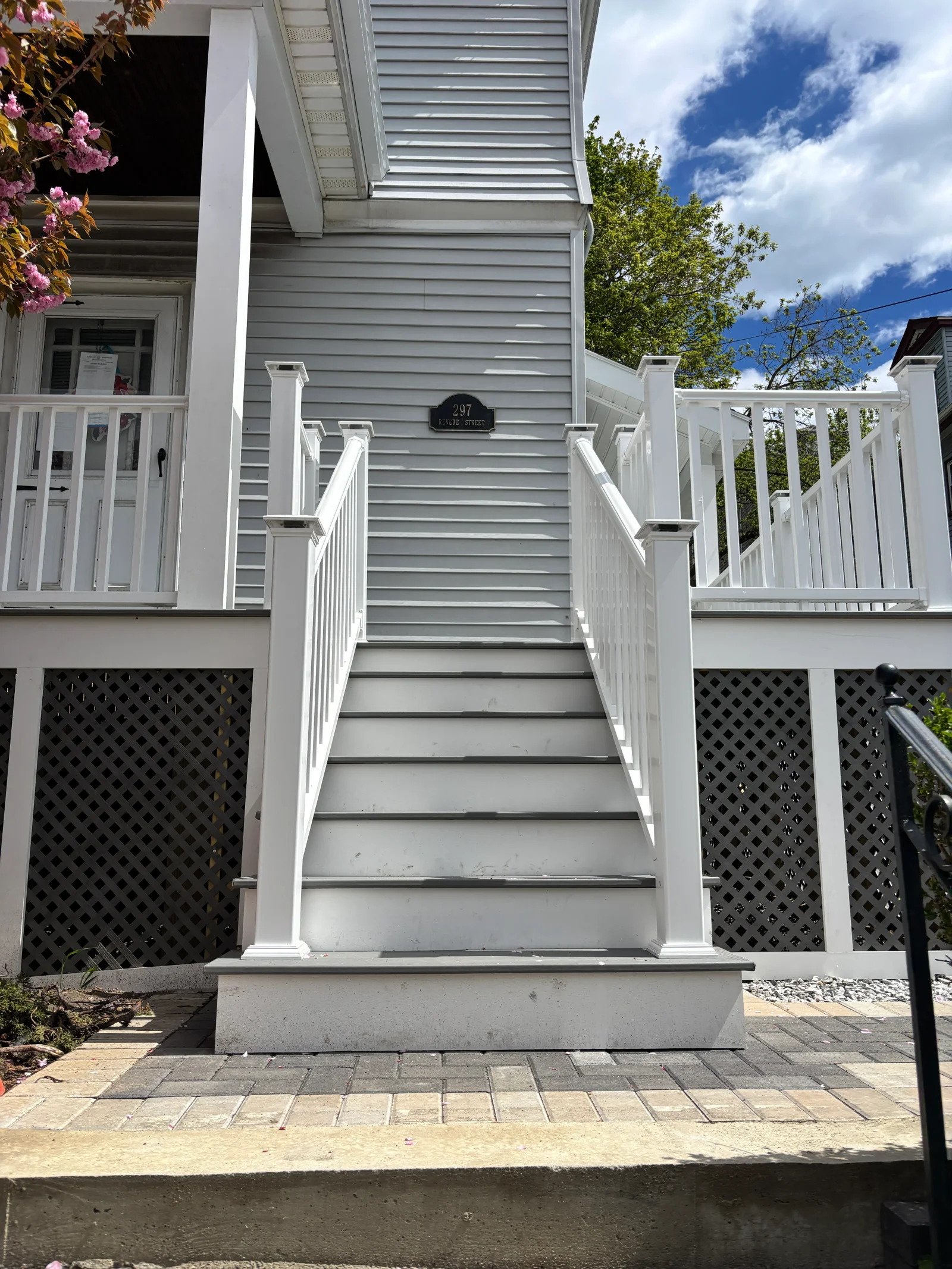 Gray composite exterior stairs with white vinyl railings, capped newel posts, and black lattice skirting below porch
