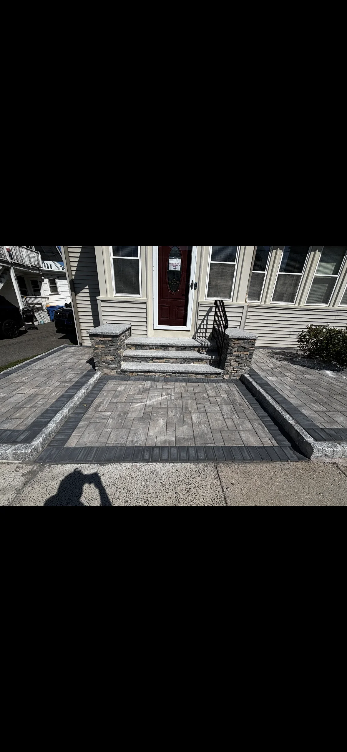 Gray paver entry walkway with dark paver border, granite curbing, granite steps, and stacked stone pillars with granite caps