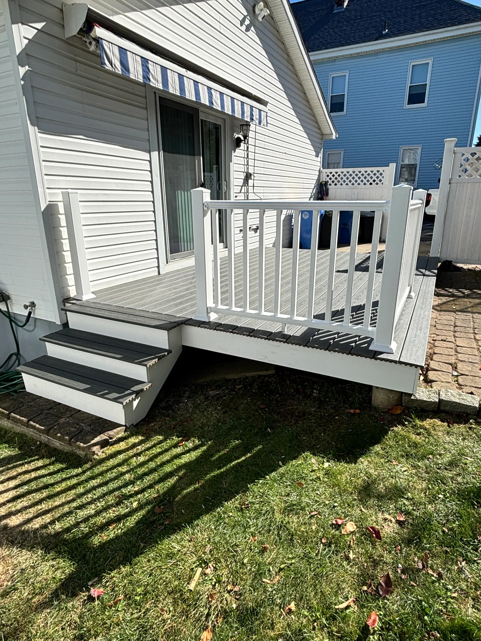 Gray composite deck with dark gray border boards, white vinyl railing, and three-step stair beside white vinyl siding