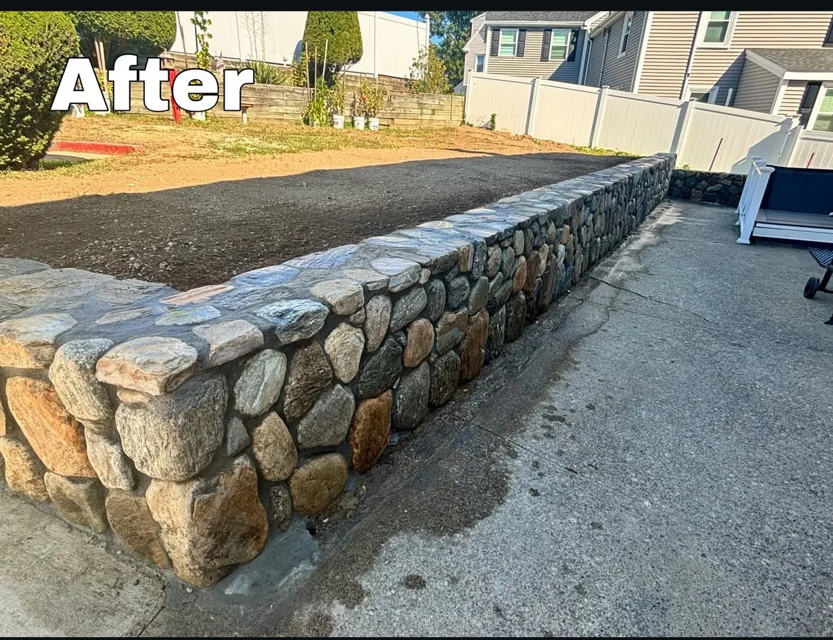 Fieldstone retaining wall with mixed-tone rounded stones and flat capstones beside a graded gravel yard and concrete patio
