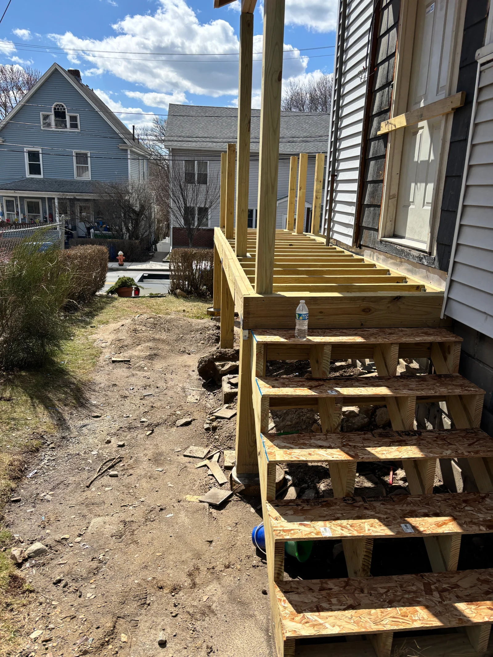 Pressure-treated lumber deck framing with posts, joists, and OSB stair treads under construction beside a house