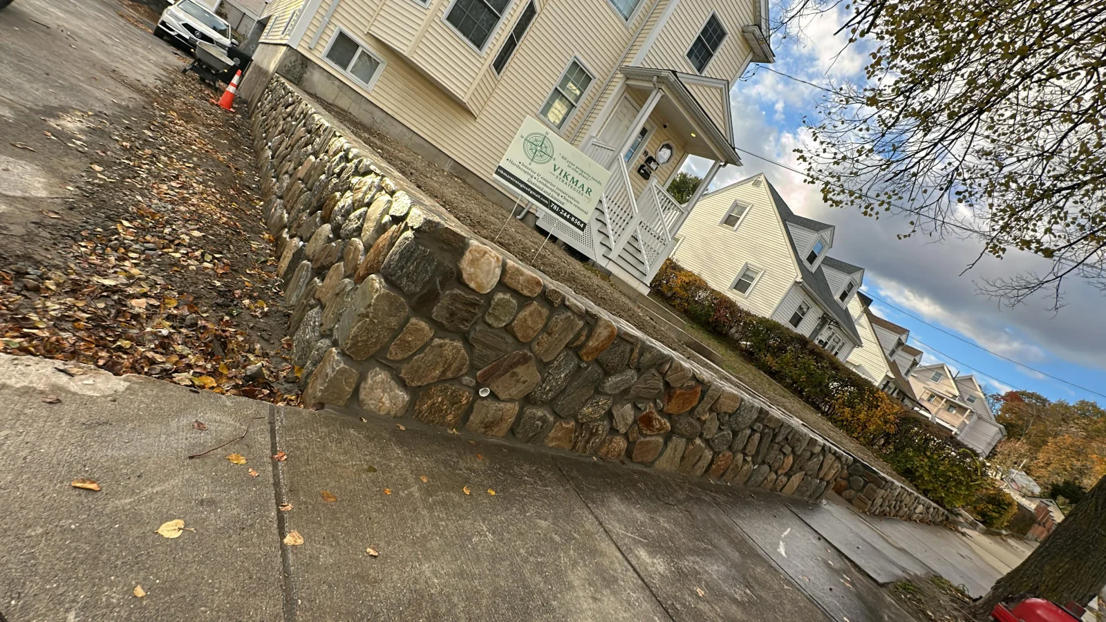 Irregular fieldstone retaining wall with a flat cap stone beside a concrete sidewalk and sloped lawn
